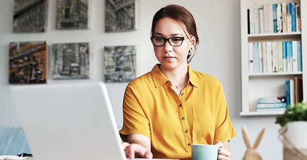 Kvinne ser på datamaskin mens hun holder en kopp, til illustrasjon for efaktura