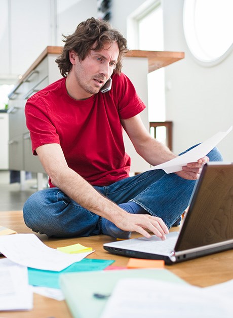 Mann sitter på gulvet og jobber på pc, til illustrasjon for ulike lånetyper