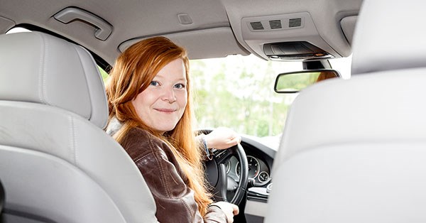 Jente sitter i bil og holder i rattet, til illustrasjon for kjøpe eller lease bil
