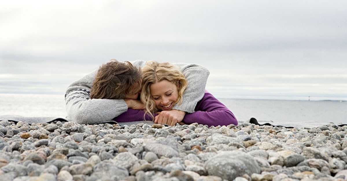 Par ligger på stranda ved havet og klemmer, til illustrasjon for samboerkontrakt