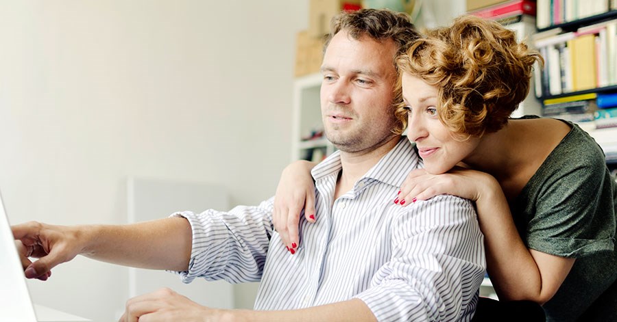 En mann viser noe på PC skjerm til en kvinne som lener seg på han, til illustrasjon for finansieringsbevis