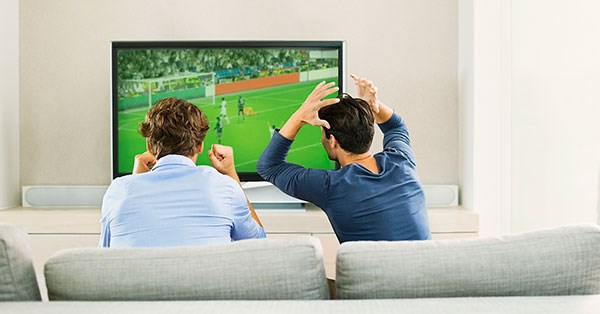 To kompiser sitter i sofa og ser fotballkamp, til illustrasjon for kjøpe bolig med en venn