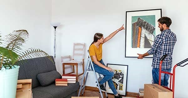 Ungt par har kjøpt bolig sammen og sitter i stua og henger opp bilder på veggen