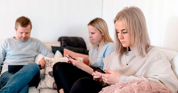 Mann med PC og to unge jenter med mobilen sitter i sofa, til illustrasjon for på vei inn i voksenlivet