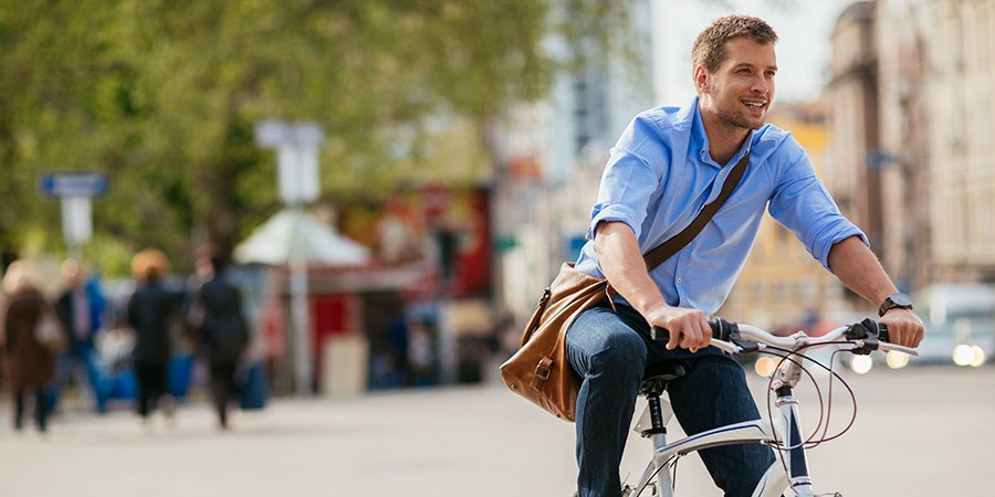 Mann i blå skjorte og veske sykler rundt i byen, til illustrasjon for høyrentekonto