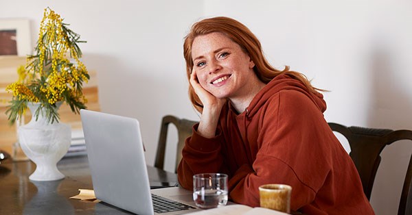 Ung jente sitter på kjøkkenbord med datamaskin fremfor seg og smiler, til illustrasjon for sparekalkulator