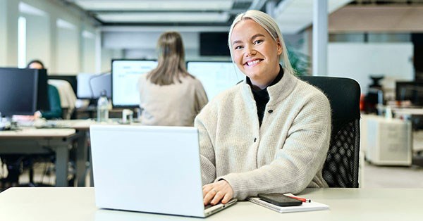 Kunderådgiver Emilie sitter på kontorplass med PC og smiler, til illustrasjon for sparing
