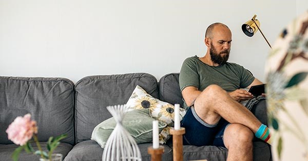 Mann sitter i sofa i eget hjem og leser på nettbrett, til illustrasjon for gjeldsregisteret