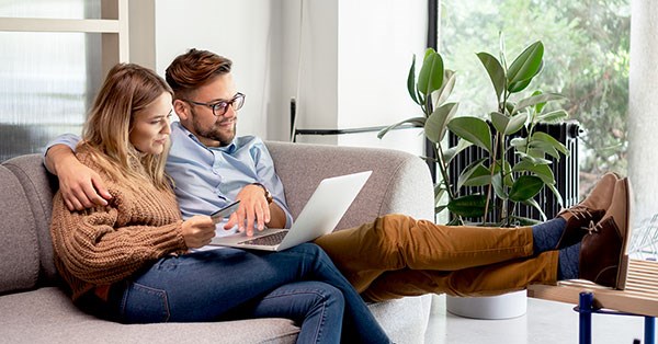 Par som sitter i sofaen og ser på laptop, til illustrasjon for omkostninger ved boligkjøp